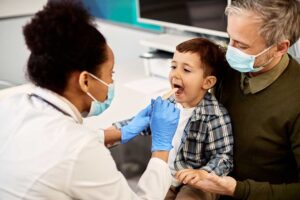 A young child brushing their teeth at a bathroom sink with a parent supervising closely.