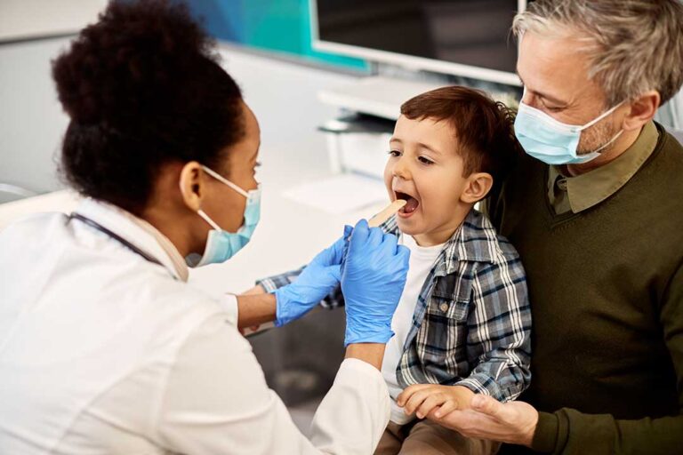 A young child brushing their teeth at a bathroom sink with a parent supervising closely.