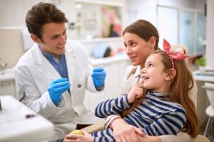 A child smiling and speaking with an adult while holding a toothbrush in a bright home setting.