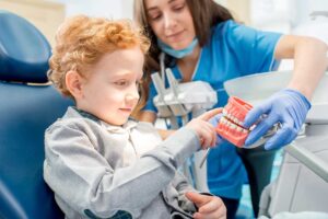 Child seated in a dental chair while a hygienist gently cleans their teeth with a caregiver nearby